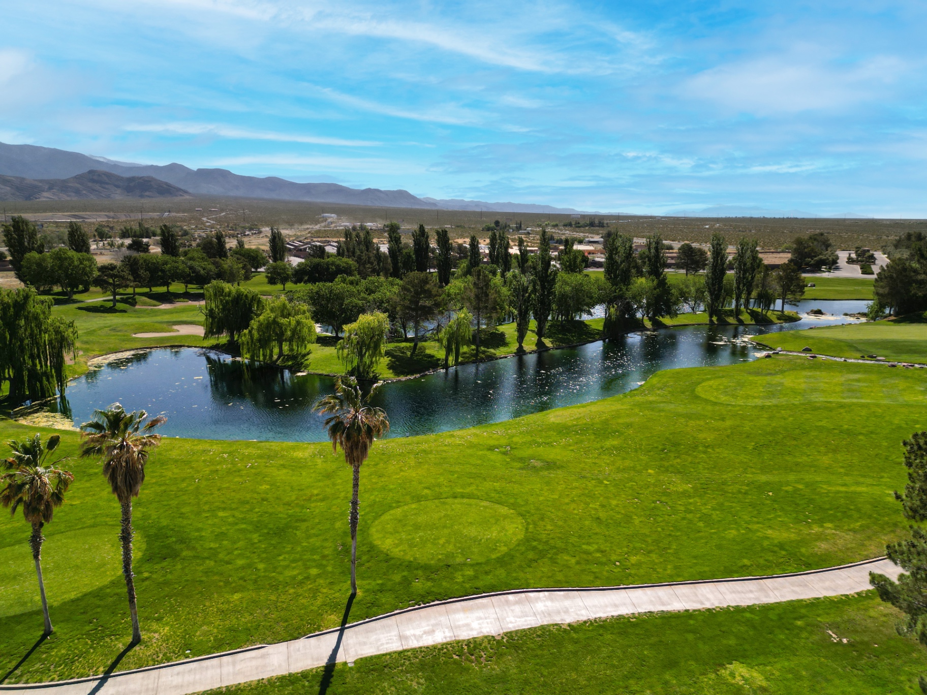 Aerial view of a Pahrump golf course with ponds, palm trees, and mountains in the distance